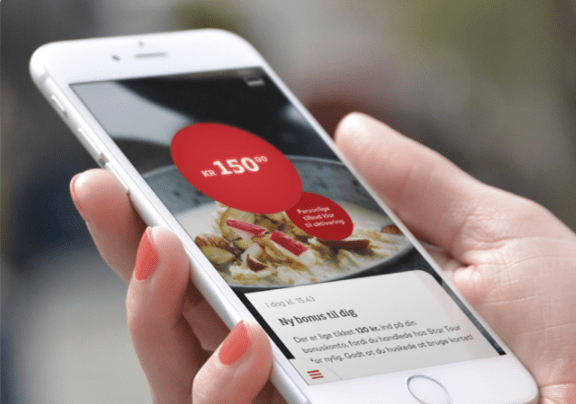 Kvinde med lyserød neglelak viser Coop-appen på sin smartphone og har 150 kroner i bonus.